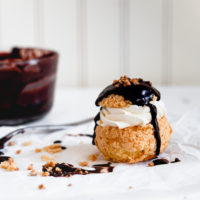 Gluten Free Choux au Craquelin filled with creme chantilly and topped with hot fudge sauce and candied hazelnuts