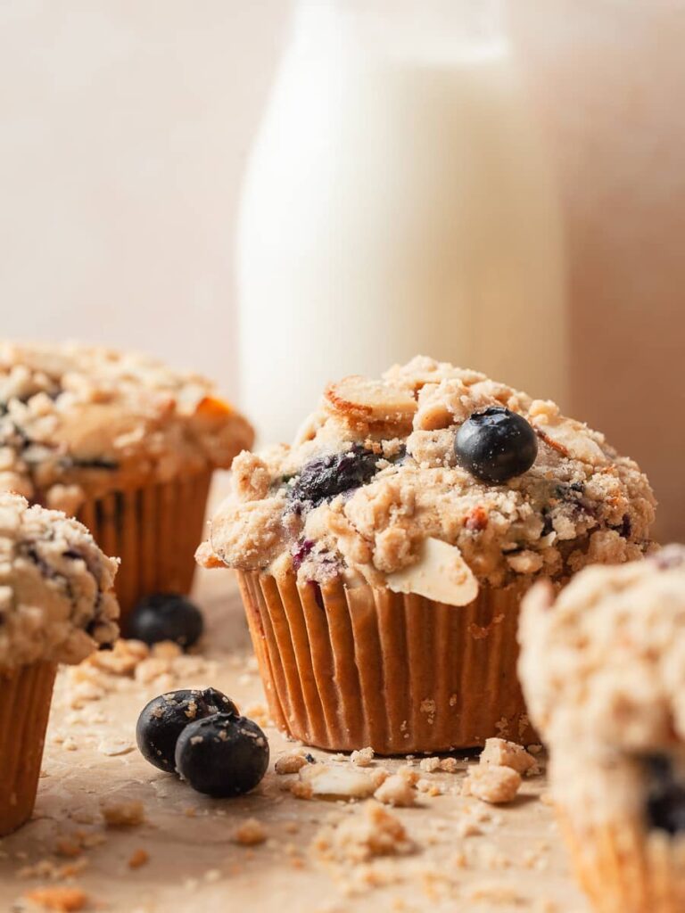 A gluten free blueberry muffin with streusel topping and a bottle of milk in the back