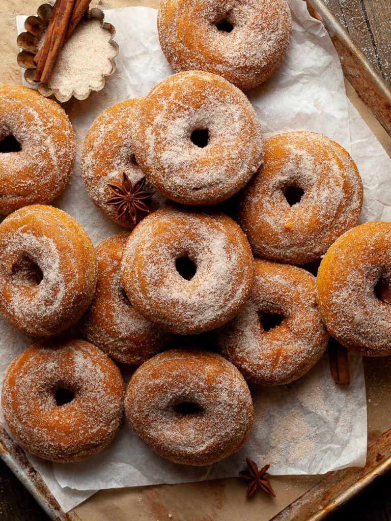 a pile of gluten free baked pumpkin donuts on a sheet tray
