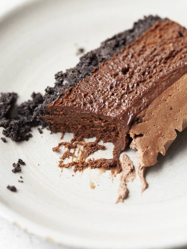 A slice of gluten-free chocolate cheesecake with oreo crust, dark chocolate filling and chocolate whipped cream