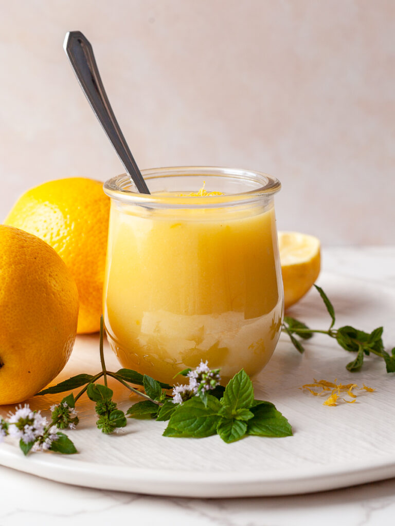 a jar of gluten-free lemon curd on a white plate with lemons and fresh mint