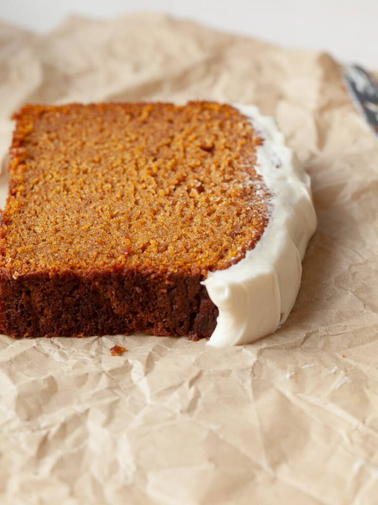 a slice of gluten free pumpkin bread topped with cream cheese frosting on brown parchment paper