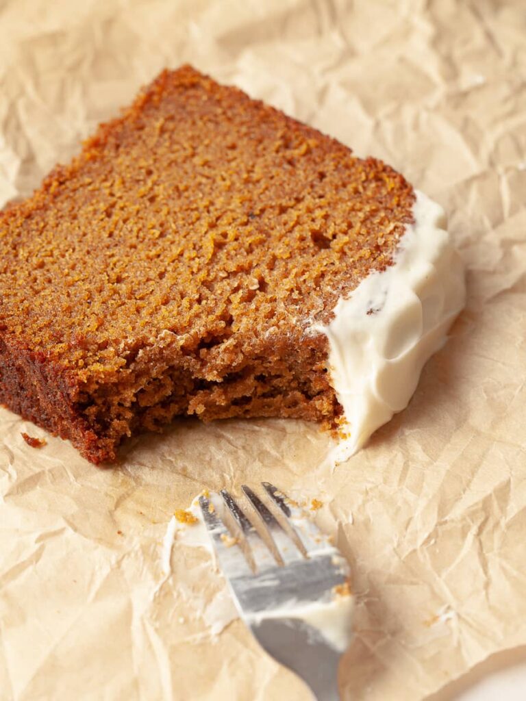 a slice of pumpkin bread on parchment paper with one bite taken out. dirt fork