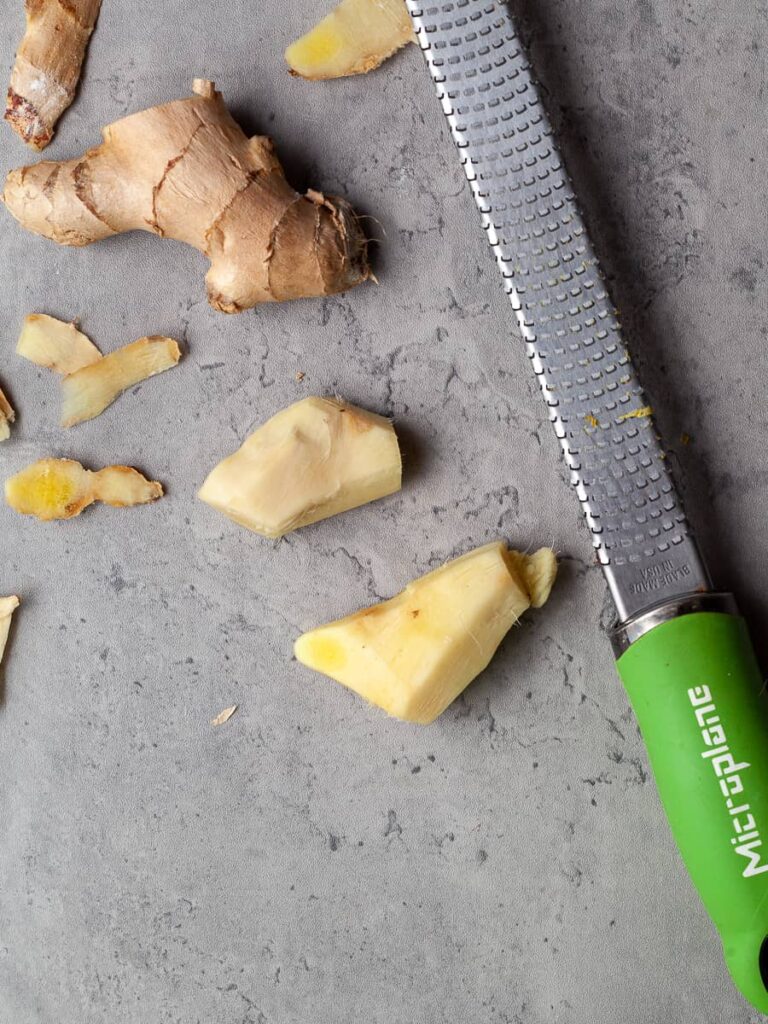 peeled fresh ginger on a gray backdroop with a microplane