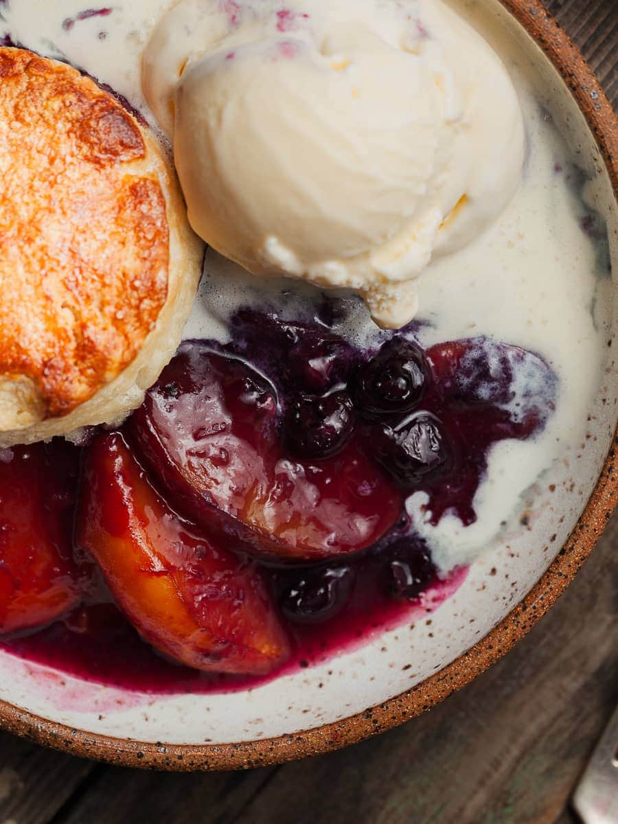 a close up of cooked peaches and blueberries with ice cream and a gluten free biscuits