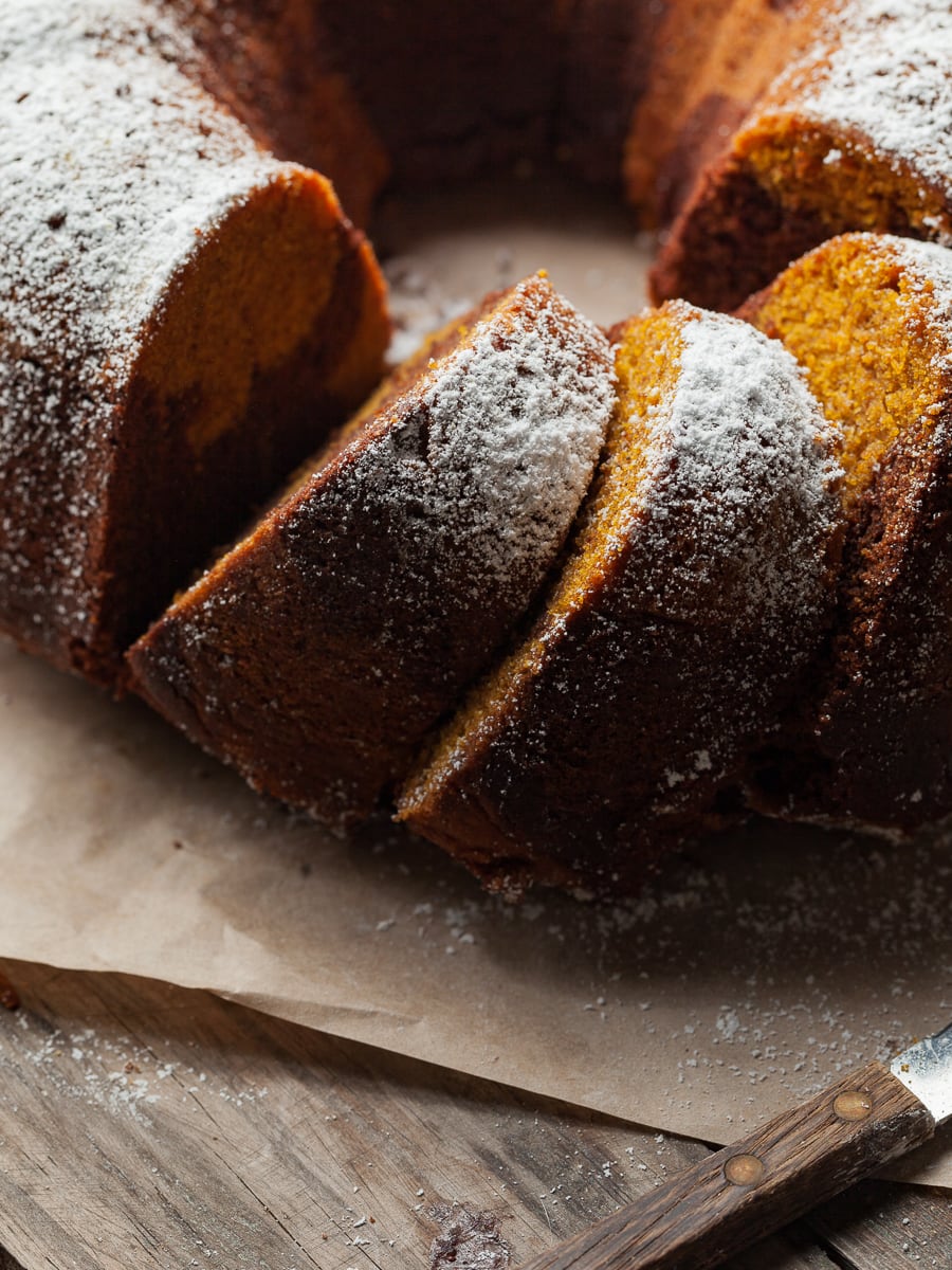 a gluten free pumpkin bundt cake with chocolate swirl on a brown parchment paper dusted with powdered sugar