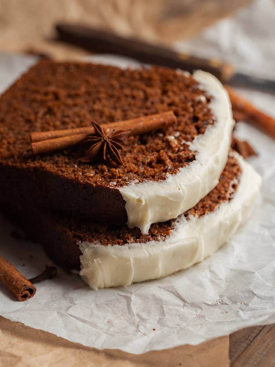 stacked slices of gingerbread loaf with cream cheese frosting, topped with a cinnamon stick and star anise