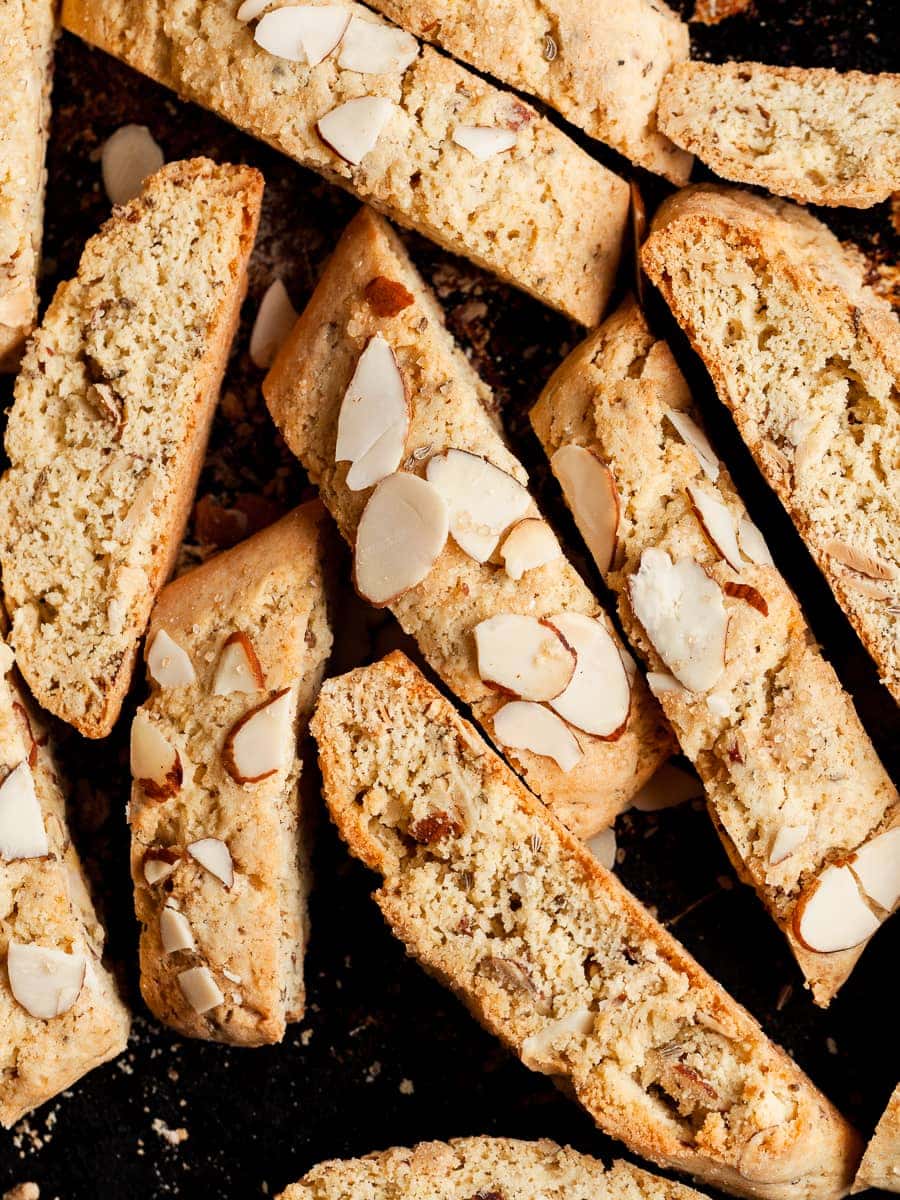 Gluten Free Almond Biscotti topped with toasted sliced almonds on a dark sheet tray.