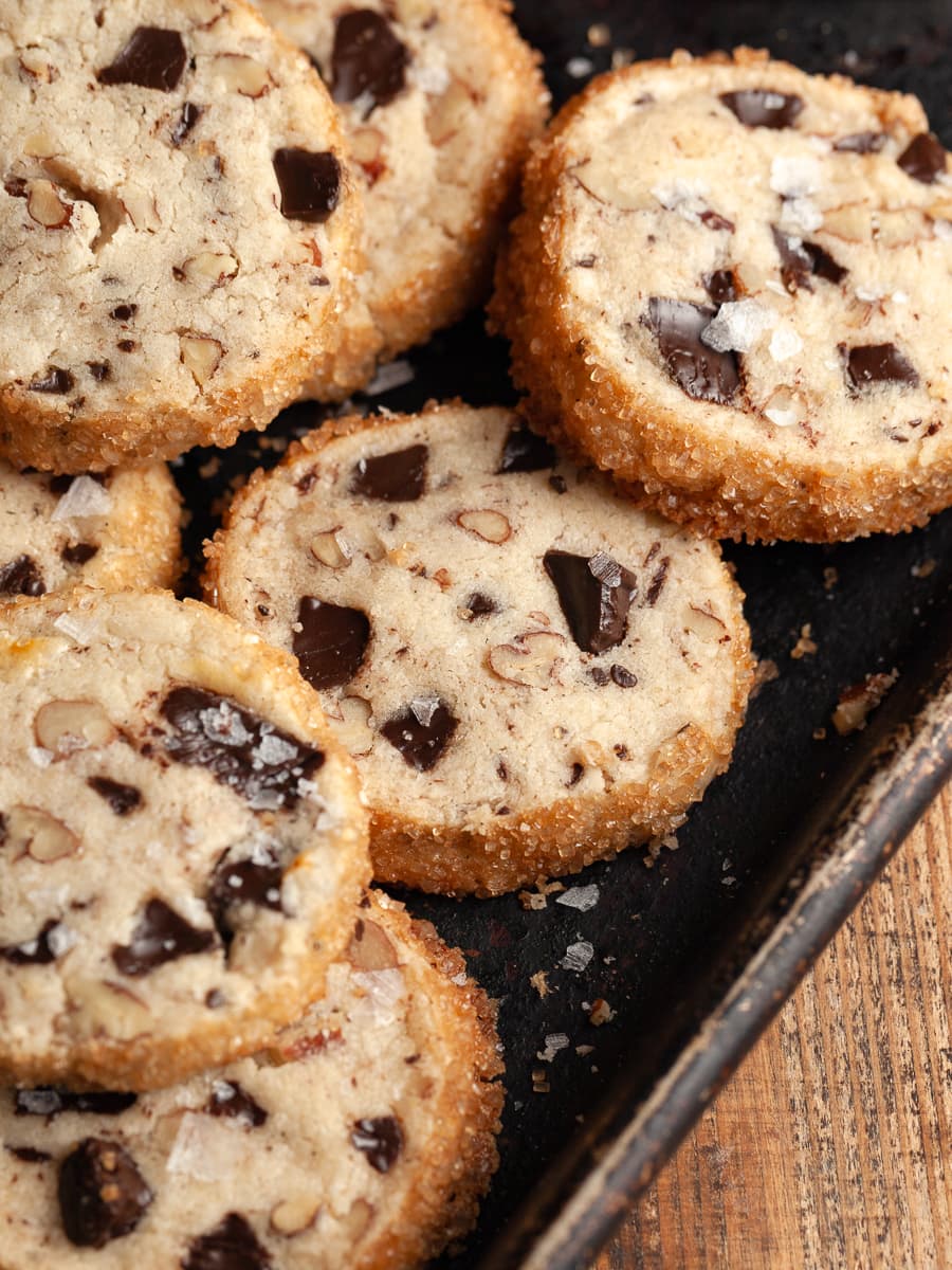 pecan shortbread cookies with dark chocolate chunks and flaky sea salt on a dark sheet tray