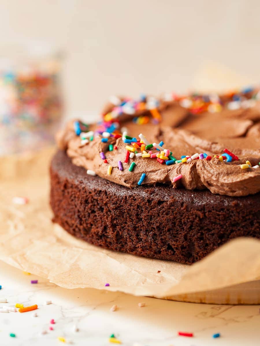 gluten free sourdough chocolate cake with a chocolate frosting and topped with sprinkles on parchment paper
