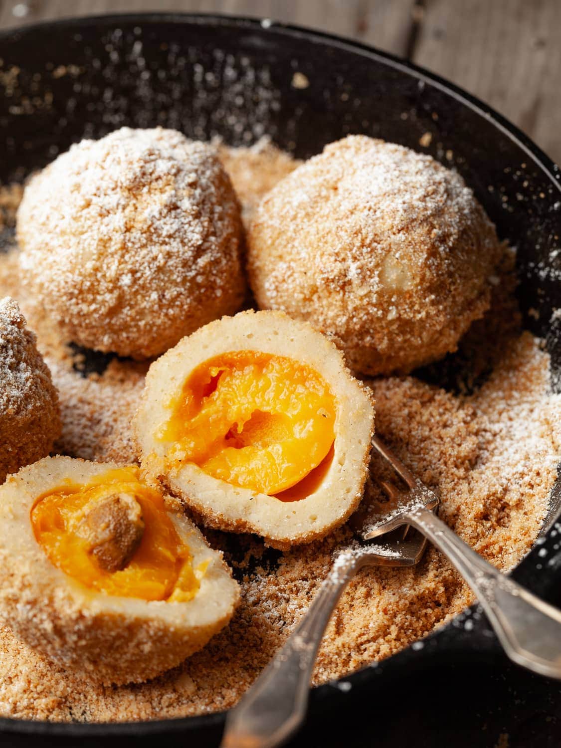 Gluten Free Marillenknödel (Austrian Apricot Dumplings) topped with bread crumbs and powdered sugar in a cast iron pan