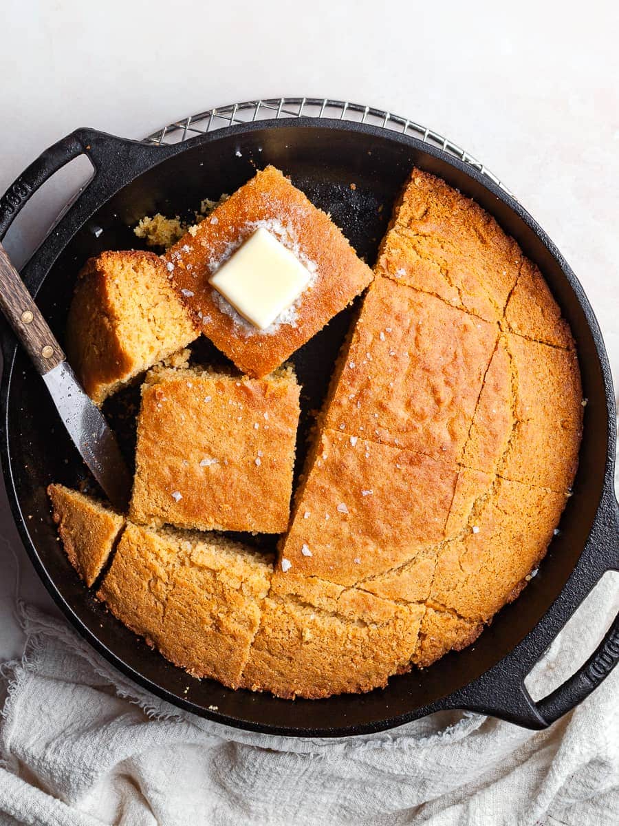 a sliced gluten free cornbread baked in a skillet, topped with melted butter and flaky sea salt, gluten free skillet cornrbread