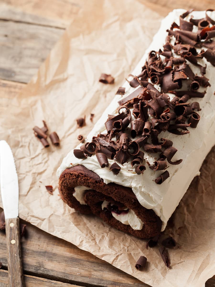 gluten free chocolate swiss roll filled with cherry jam and whipped cream. topped with whipped cream and chocolate curls, black forest swiss roll