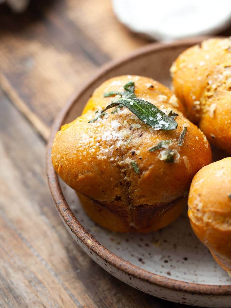 gluten free pumpkin dinner rolls on a plate, topped with flaky sea salt and crispy sage