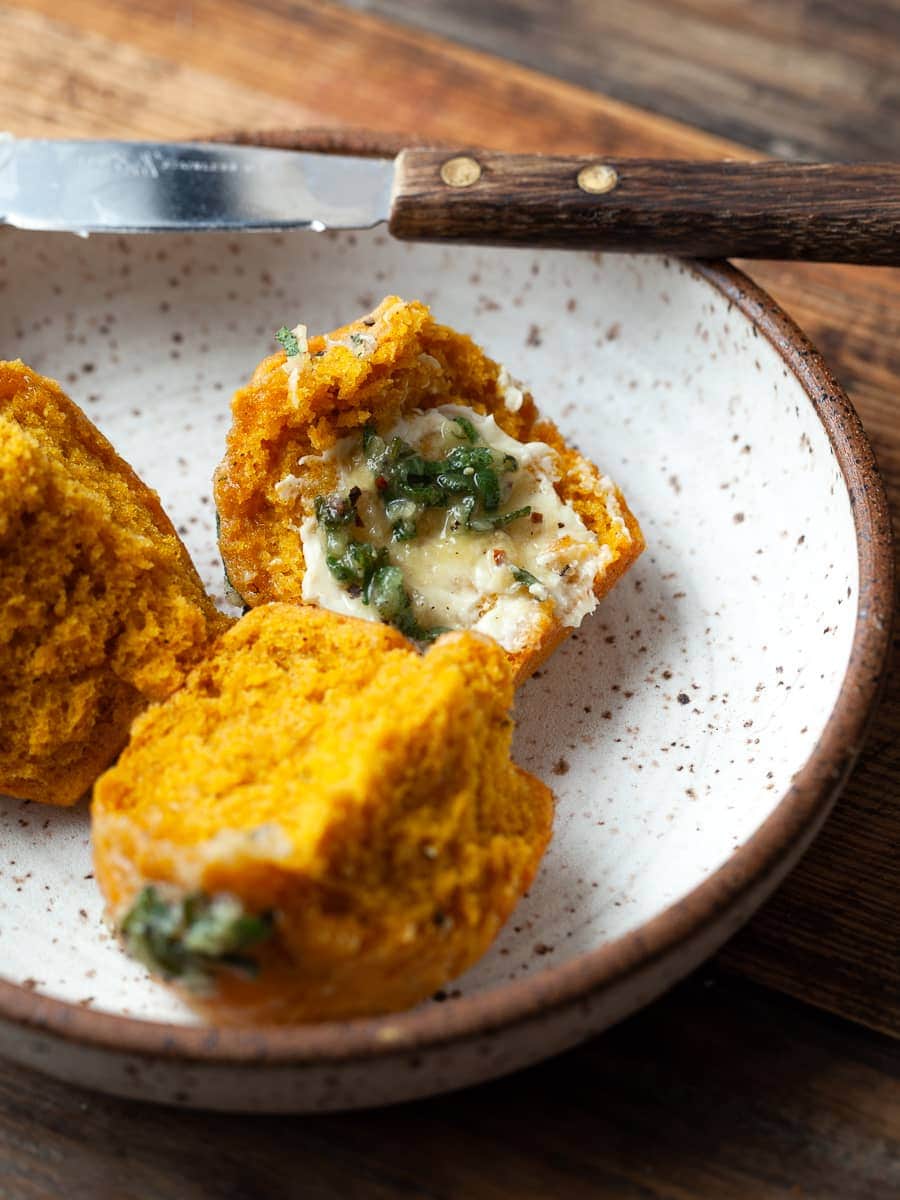 a pumpkin dinner roll on a plate topped with butter and sage with a small knife in the back