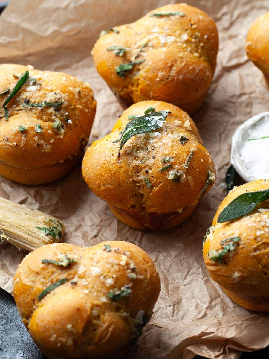 gluten free pumpkin dinner rolls on a plate topped with flaky sea salt and crispy sage