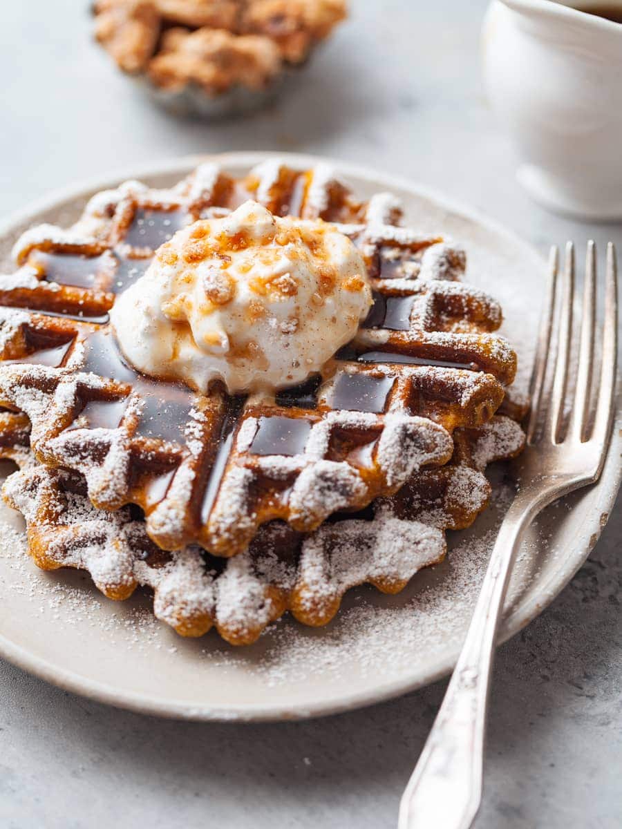 gluten free pumpkin waffles topped with whipped cream, maple syrup and crushed walnuts on a plate