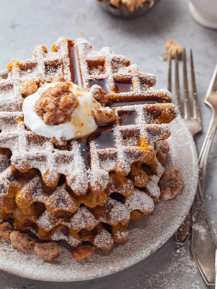 gluten free pumpkin waffles topped with whipped cream, maple syrup and crushed walnuts on a plate