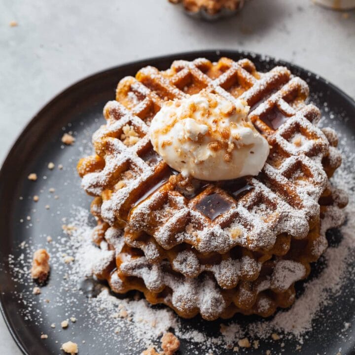 gluten free pumpkin waffles topped with whipped cream, maple syrup and crushed walnuts on a plate