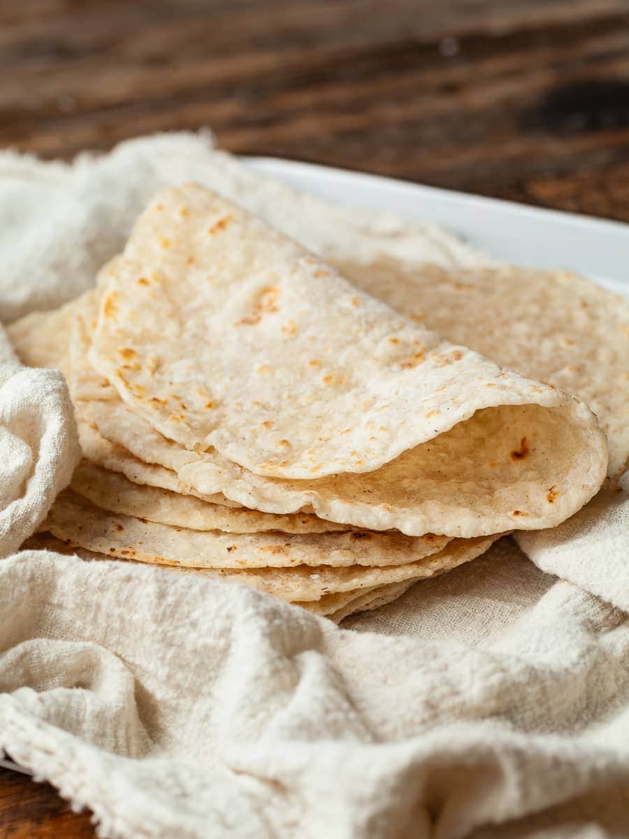 gluten free flour tortillas stacked on a kitchen towel, one tortilla folded over 