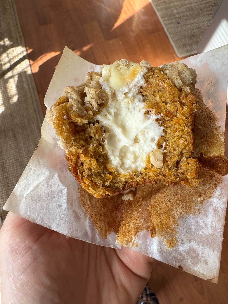 a bite taken out of a gluten free carrot cake muffin with cream cheese filling