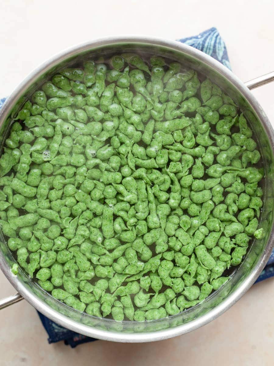 Gluten Free Spinach Spätzle floating in hot water in a pot