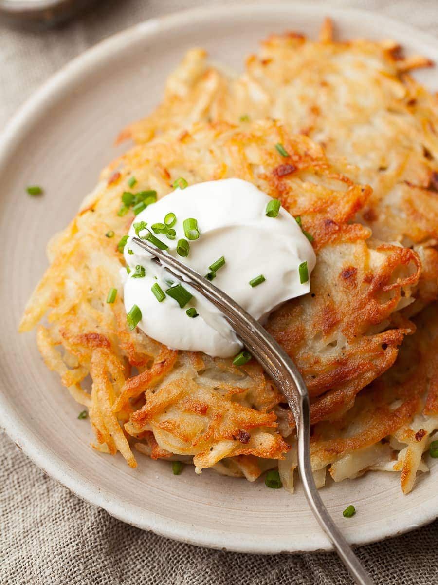 crispy gluten free potato pancakes topped with sour cream and chives and a fork