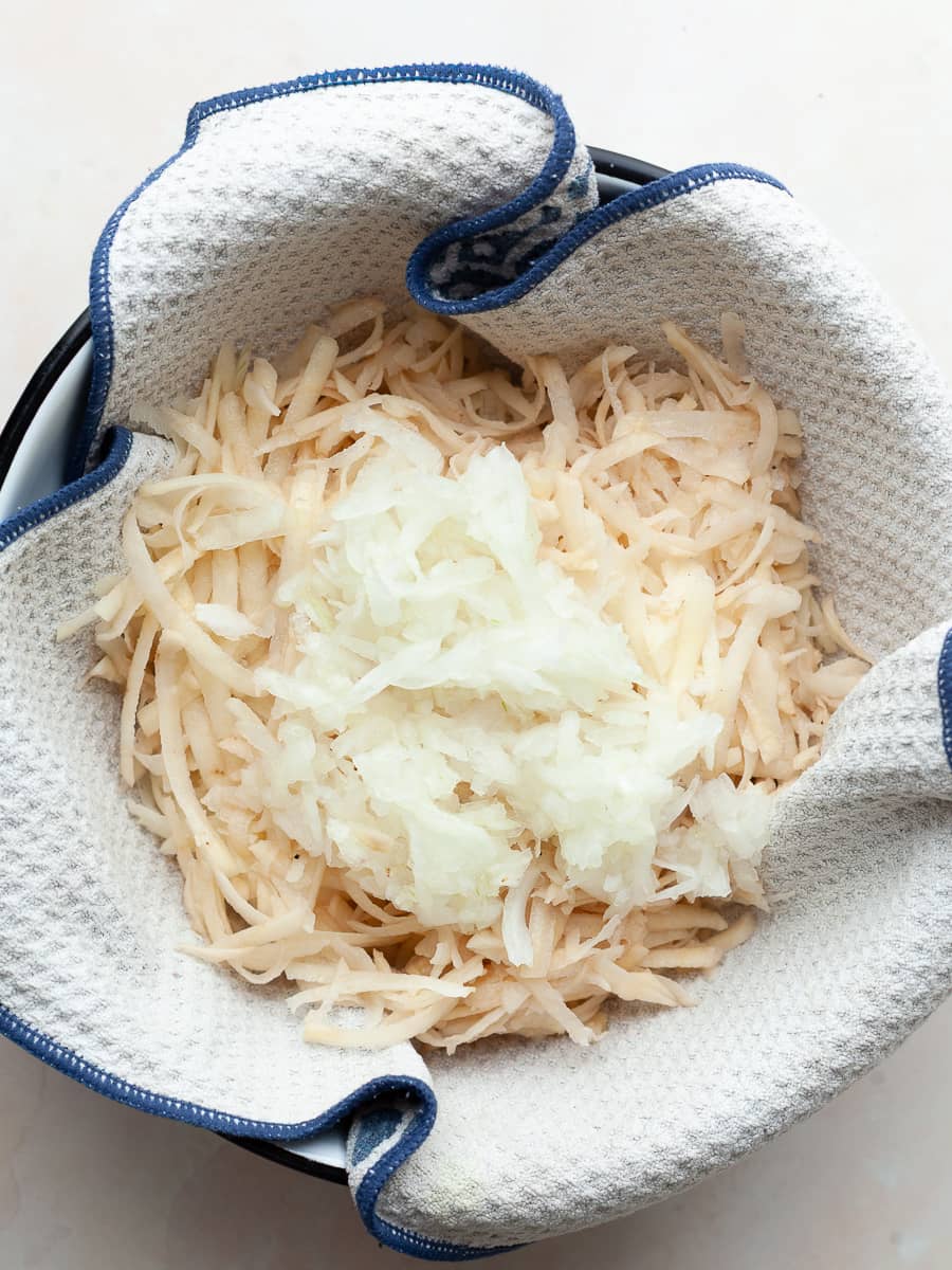grated onions and potatoes in a bowl lined with a clean towel for potato pancakes