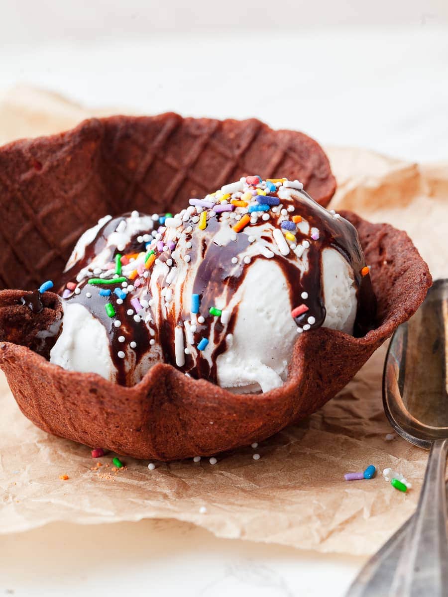 a gluten free chocolate waffle cone bowl with vanilla ice cream, hot fudge sauce and sprinkles