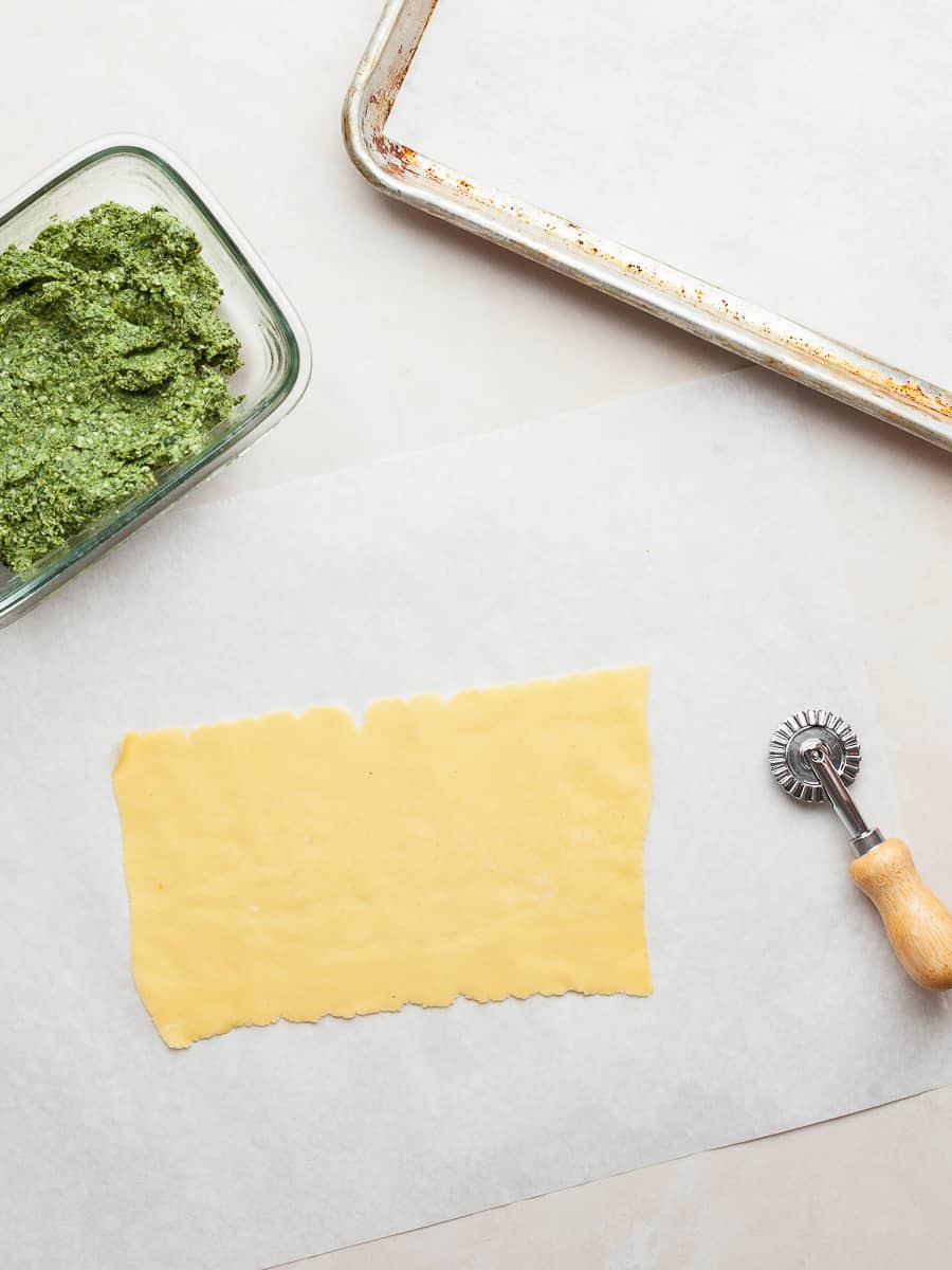 a sheet of gluten free pasta, a container with spinach ricotta ravioli filling and a pastry cutter on a table