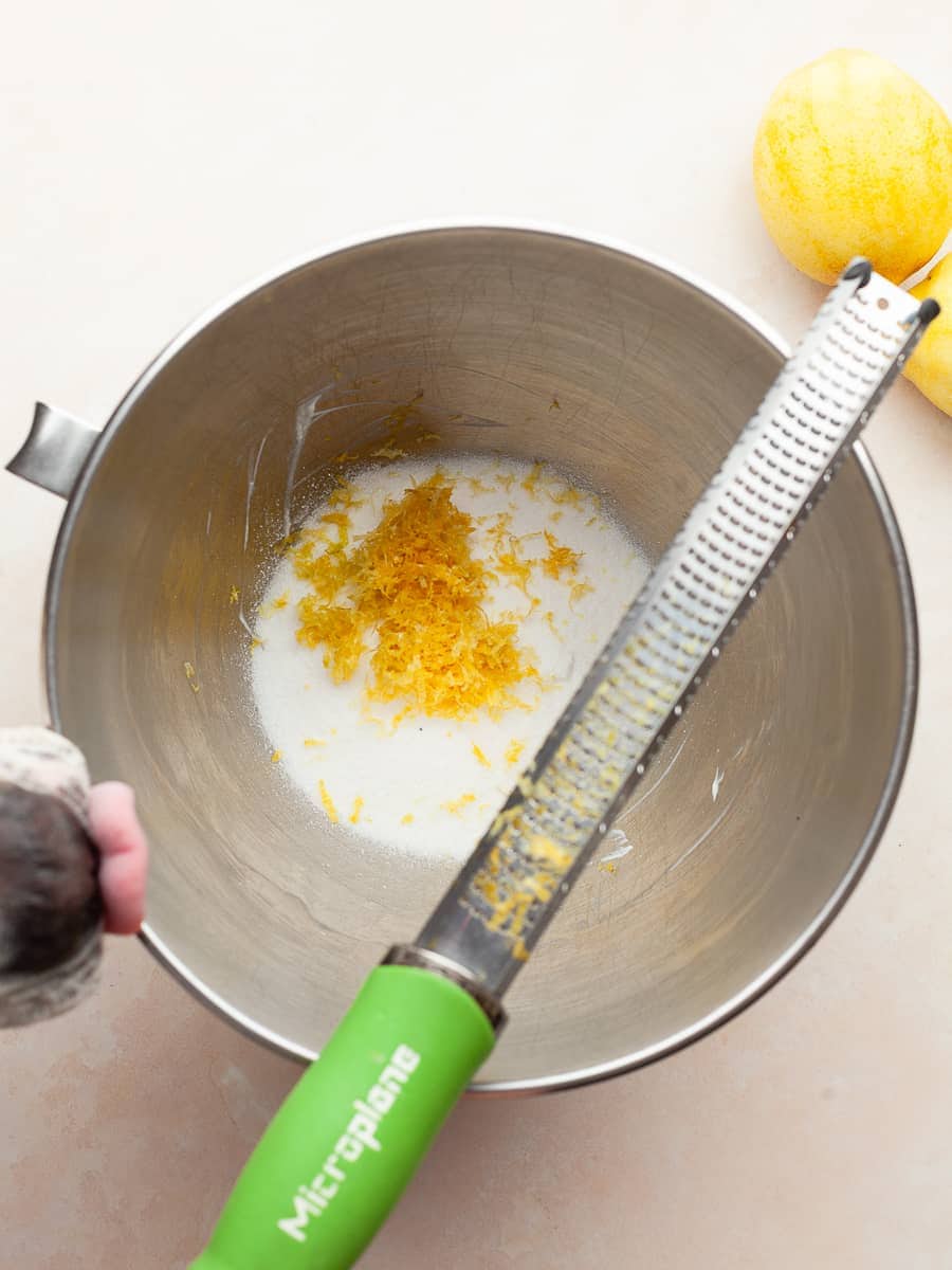 bowl of stand mixer with granulated sugar and lemon zest and a microplane across the bowl