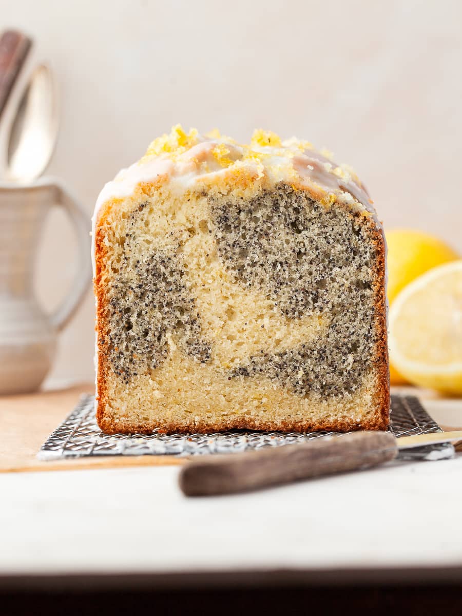 a gluten free lemon poppy seed loaf on a cooling rack topped with lemon glaze and lemon zest, a few lemons in the back
