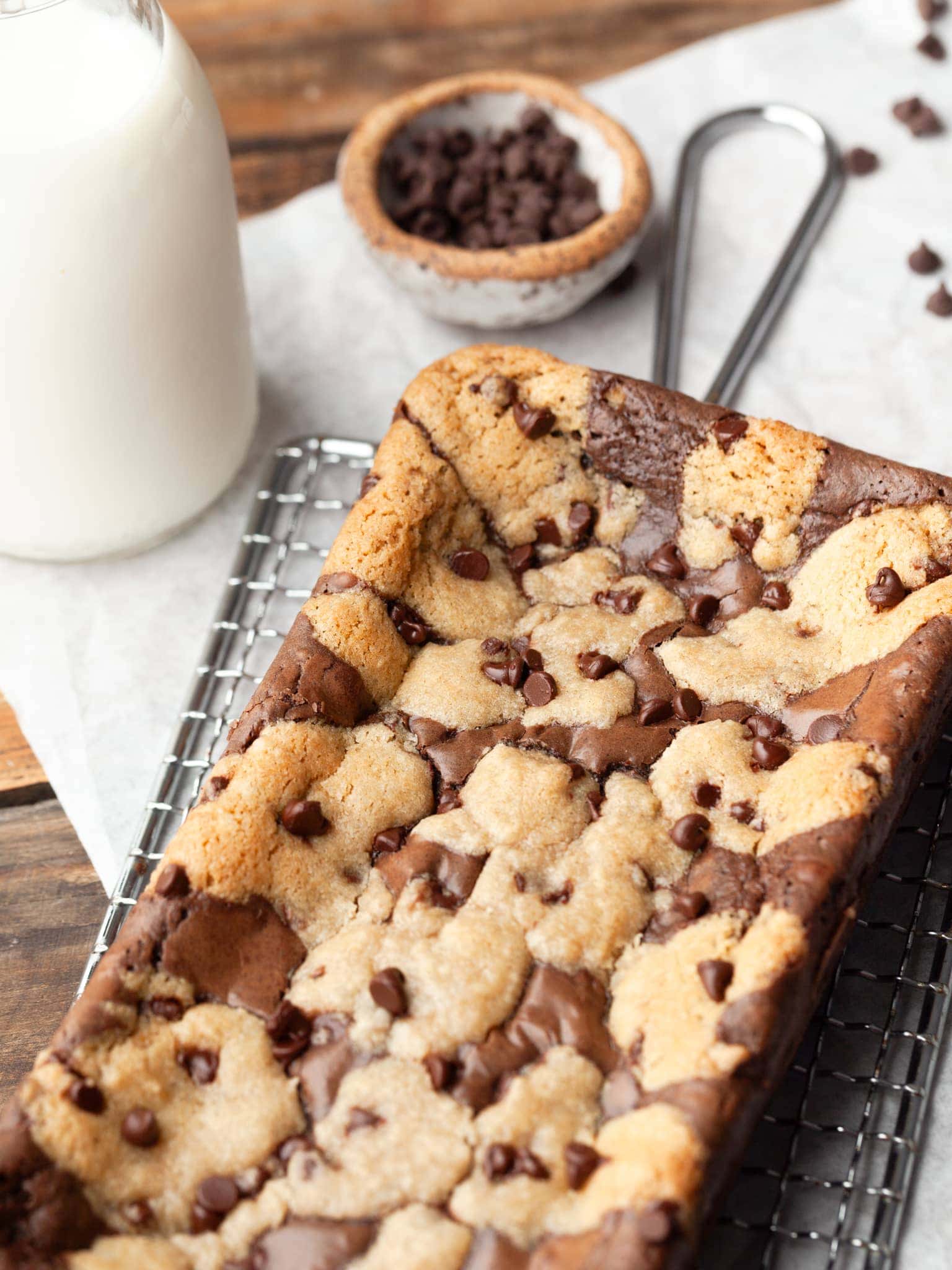 gluten free brookies topped with chocolate chips on a cooling rack with a small knife and bowl of chocolate chips